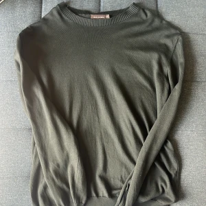 Mörkgrön tröja från Oscar Jacobson XL - Stilren mörkgrön tröja från Oscar Jacobson i storlek XL. Tröjan har rund halsringning med ribbade detaljer och långa ärmar. Perfekt för dig som gillar en klassisk och enkel look. Materialet känns mjukt och passar bra till lager-på-lager.