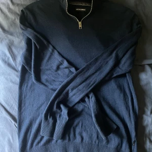 Mörkblå Grisch Tröja - Mörkblå långärmad tröja från Jack & Jones med half zip-dragkedja vid halsen. Tröjan är stickad och har ribbade muddar vid ärmslut och nederkant. Perfekt för lager-på-lager och enkel att matcha med jeans eller chinos.