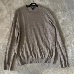 Beige slim fit tröja från H&M - En stilren beige tröja från H&M i slim fit-modell. Tröjan har rund halsringning, långa ärmar och ribbade muddar vid ärmslut och nederkant. Perfekt för lager-på-lager och enkel att matcha med olika outfits.
