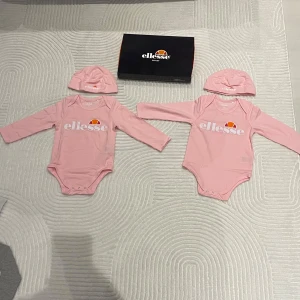 : Ellesse baby set 12-18 mån -  Baby set från Ellesse – body/overall + mössa. Finns i rosa  Storlek: 12-18 månader. Alla helt nya med taggar kvar och i originalförpackning.