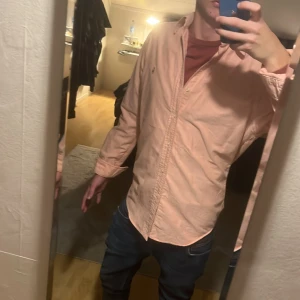 Rosa skjorta från Ralph Lauren - Säljer en snygg rosa skjorta från Ralph Lauren i slim fit-modell. Skjortan har klassisk krage, knäppning framtill och den ikoniska broderade loggan på bröstet. Tillverkad i bomull och har långa ärmar. Perfekt för dig som vill ha en stilren och fräsch look. Storlek medium med en slim fit som gör att den blir som Small