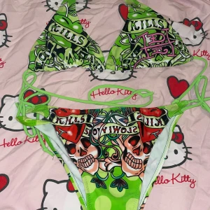 Grön Ed Hardy bikini med dödskallar - Snygg trekantsbikini från Ed Hardy i grönt med färgstarkt tatueringsinspirerat tryck, dödskallar och hjärtan. Bikinin har knyt i sidorna och i nacken för perfekt passform. Perfekt för dig som vill sticka ut på stranden!