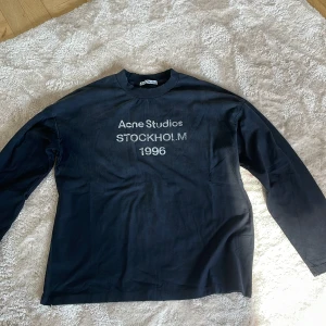 Svart långärmad tröja Acne Studios - Svart långärmad tröja från Acne Studios med tryck 'Acne Studios STOCKHOLM 1996' på bröstet. Tröjan har en klassisk rund halsringning och är tillverkad i mjuk bomull. Perfekt för en clean och stilren look.