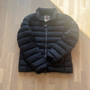 Svart pufferjacka från Colmar - Säljer en svart pufferjacka från Colmar med hög krage och dragkedja framtill. Jackan har ett stilrent, quiltat mönster och Colmar-logga på ärmen. Perfekt för kyliga dagar och enkel att matcha med olika outfits.