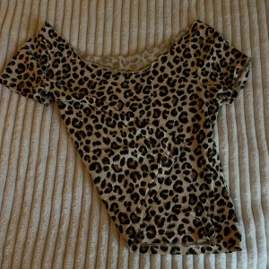 Leopardmönstrad topp med kort ärm - Säljer en snygg topp med leopardmönster i beige, svart och bruna toner. Modellen har korta ärmar och en något bredare halsringning. Perfekt för dig som vill sticka ut med ett djurmönster. Materialet känns mjukt och stretchigt, troligtvis bomull eller polyester.