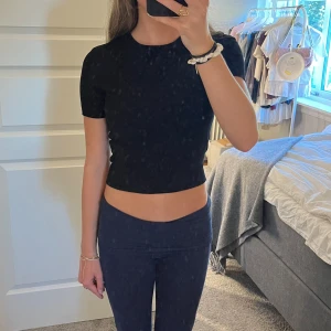 Svart croppad ribbad topp - En svart T-shirt med korta ärmar och rund hals. Toppen har en tight passform som sitter snyggt på kroppen. 