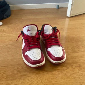 Nike Air Jordan 1 Low röd/vit/svart - Säljer ett par Nike Air Jordan 1 Low i klassisk röd, vit och svart färg. Skorna har röd snörning, perforerad tåbox och ikoniska Jordan-loggor på plösen och hälen. Tillverkade i skinn med låg profil och rund tå. Perfekta för dig som vill sticka ut med en tidlös sneaker.