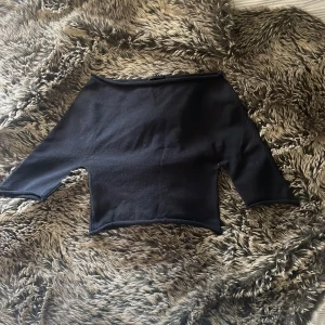 Svart offshoulder topp från Sisley - Svart offshoulder topp från Sisley med minimalistisk design och croppad passform. Tillverkad i mjuk bomull med lätt stretch. Ärmarna är korta och toppen har en stilren, enkel look som är lätt att matcha med olika outfits.