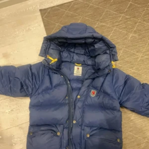 Blå Fjällräven jacka  - Jag säljer min fina fjällräven jacka som endast är använd en vinter, så därför mycket god kvalitet på den. Inget slitage eller hål, dock innerfickan har lossnat på ena sidan men den går enkelt att fixa om man vill.😊 Men size S, nya modellen.😊