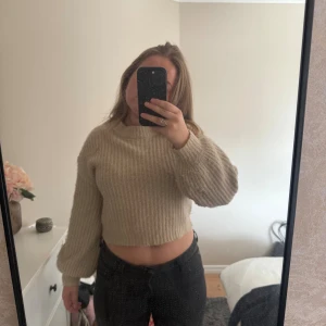 Beige croppad stickad tröja - Säljer en beige croppad stickad tröja med rund halsringning och ballongärmar. Tröjan har en ribbad struktur och är perfekt för lager-på-lager under höst och vinter. Supermjuk och enkel att styla med både jeans och kjol. Mycket bra skick