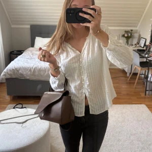 Vit randig blus från Zara - Säljer en luftig vit blus från Zara med diskreta ränder och knappar framtill. Skjortan har lång ärm, lätt v-ringning och är gjord i ett tunt, skönt bomullsmaterial. Perfekt för dig som gillar en chill och stilren vibe.