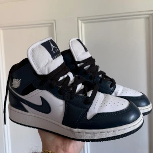 Nike Air Jordan 1 Mid vit/marinblå - Nike Air Jordan 1 Mid i vit och marinblå med svarta skosnören! Använt några gånger bara