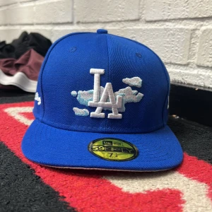 Blå LA Dodgers keps från New Era - Snygg blå 59FIFTY keps från New Era med Los Angeles Dodgers brodyr framtill och vita molndetaljer. Kepsen har platt skärm, broderad logga på sidan och MLB-märke bak. Perfekt för dig som vill sticka ut med sportig stil.
