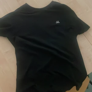 Svart t-shirt från C.P. Company - Svart t-shirt från C.P. Company med diskret logga på bröstet. Klassisk rund hals och korta ärmar. Enkel och stilren design som funkar till det mesta. Mjuk och skön bomullskvalitet.