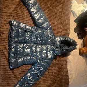 Blå glansig pufferjacka med huva - Snygg blå pufferjacka med glansig finish. Jackan har huva, dragkedja framtill och två praktiska fickor med dragkedja. Perfekt för kalla dagar. Den är ifrån Lager 157, i storlek M men passar även för dom som har större och mindre storlek. Jag är i vanliga fall en Xs-S men den här sitter fortfarande figurformad på mig och man får plats med en tjock tröja under. Använd ungefär 2-4 gånger. Nypris: 400 kr, mitt pris: 300 kr.