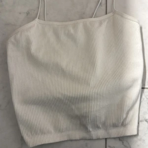 Vit ribbad linnetopp från Zara - Säljer en stilren vit ribbad linnetopp från Zara med tunna axelband. Toppen har en croppad passform och är tillverkad i ett mjukt, stretchigt material som sitter snyggt på. Använd 1 gång, köparen står för frakten :)