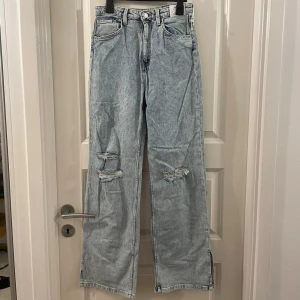 Ljusblå wide leg jeans med slitningar - Snygga ljusblå jeans med wide leg och hög midja. Jeansen har justerbar midja och slitna detaljer vid knäna för en cool look. Perfekta för dig som gillar en avslappnad och trendig stil.
