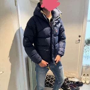 Marinblå Fjällräven Expedition dunjacka XS - Säljer en marinblå Fjällräven Expedition Series dunjacka i herrmodell, storlek XS. Jackan har huva, gula snörningsde. 