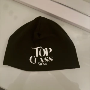 Svart mössa Top Class Music - Svart mössa med vit tryckt text 'Top Class Music' framtill. Enkel och stilren design, perfekt för dig som vill ha en clean look. Tillverkad i mjukt material som sitter skönt på huvudet.