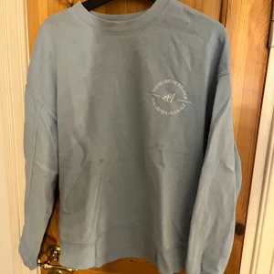 Ljusblå sweatshirt med tryck - Ljusblå sweatshirt med rund hals och tryck på bröstet.