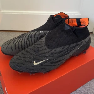 Nike Phantom GX Elite Fotbollsskor - Riktigt snygga fotbollsskor i ”Phantom” modellen som inte tillverkas längre.  De är endast testade några träningar och har därav inga skavanker alls.  Snöret göms under tyget och materialet på majoriteten av skon är i Nikes ”Gripknit” tyg som gör att man får bättre grepp på bollen.  Storlek 45 / US 11 / UK 10 
