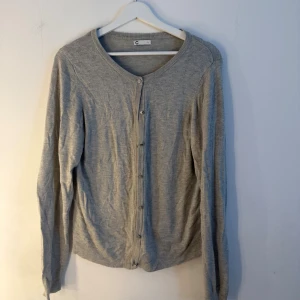 Grå kofta  - Grå kofta med långa ärmar och knäppning framtill. Rund halsringning. Storlek L