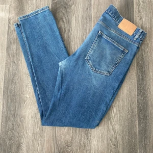 Blå jeans från Dobber W33 L32 - Klassiska blå jeans från Dobber med raka ben och normal passform. Jeansen har snyggt slitna detaljer framtill och bak, samt en ljus tvätt. Perfekt för en stilren look.