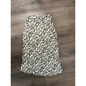 Beige långkjol med ormmönster - Säljer en beige och svart kjol som går ner till halva vaderna. Lite mermaid passform  med coolt ormmönster., lätt material som faller snyggt. 