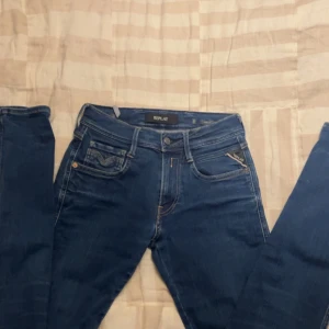 Blå Replay Anbass jeans, - Snygga blå Replay Anbass jeans med klassisk femficksdesign, gul kontrastsöm och läderpatch bak. Jeansen är slim fit och är tillverkade i stretchigt denim för extra komfort. Perfekta för dig som gillar stilrena och tidlösa jeans med coola detaljer.