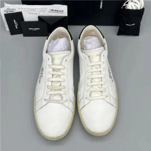 Saint Laurent vita sneakers i skinn - Snygga vita sneakers från Saint Laurent i skinn med svart detalj på hälen och handskriven logga på sidan. Klassisk låg modell med rund tå, platt sula och snörning. Perfekta för dig som gillar stilrena och exklusiva skor med en cool touch.