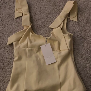 Gul linnetopp med rosetter från Zara - Supersöt ljusgul linnetopp från Zara med breda axelband och fina rosettdetaljer på axlarna. Toppen har lappen kvar då jag aldrig använt den, så super bra skick. Ordinarie pris är 329 (lappen) men jag kommer sälja den för 259 kr ❤️💛