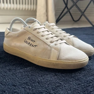 Saint Laurent vita sneakers - Snygga vita sneakers från Saint Laurent med handskriven logga på sidan. Skorna har klassisk snörning samt platt sula. Perfekta för dig som gillar minimalistisk och stilren design. Inget dåligt med skorna inga hål någon stans
