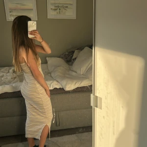 Randig ribbad tubklänning i beige - Säljer en ribbad, ärmlös tubklänning i beige med tunna bruna och vita ränder. Klänningen är lång, har en slits på sidan och sitter tight mot kroppen 💗står ingen storlek men skulle säga s typ