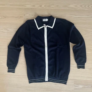 Mörkblå kofta från OXKNIT med vita detaljer - Snygg mörkblå kofta från OXKNIT med vita ränder längs krage, dragkedja och muddar. Koftan har långärmad design, ribbade muddar och klassisk krage. Perfekt för dig som gillar stilrena och sportiga vibbar. Helt ny. Lappar finns kvar. Bara att höra av sig vid frågor!