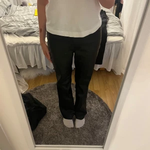 Svarta raka byxor i skinn - Säljer ett par svarta byxor i skinnimitation med raka ben och klassisk passform. Byxorna har fickor bak och en stilren look som passar perfekt till en trendig outfit. Materialet ger en cool vibe och de är lätta att matcha med olika toppar.