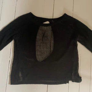 Svart stickad topp med öppen rygg - Svart stickad topp med lång ärm och coolt hålmönster framtill och i ryggen. Materialet är tunt och transparent, perfekt för lager-på-lager. Har någon lös tråd och lite uttöjda hål men för övrigt i okej skick!