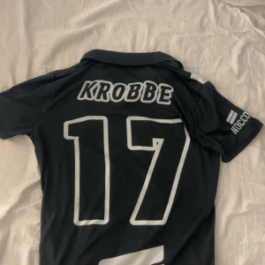 Svartvit FC Bruk fotbollströja - Jag säljer en KROBBE tröja! Den här tröjan fångade jag under en invigning där självaste Krobbe kastade ut tröjan. (Filmbevis finns) På tröjan finns NOCCOS loggor och på framsidan så står det fotbollslaget som krobbe spelade i förut. Den här säljer jag pågrund av att jag inte har användning av den. Pris går att diskuteras! 