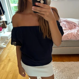 Navy blå offshoulder blus med spets - Säljer en  offshoulder blus med korta ärmar och snygga spetsdetaljer på ärmsluten. Blusen har en luftig passform och är perfekt för dig som gillar en stilren look med lite extra detaljer. Passar till både jeans och kjol för en trendig vibe.