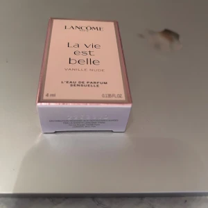 Lancome La Vie Est Belle Vanille Nude 4ml - Säljer en Lancome La Vie Est Belle Vanille Nude Eau de Parfum Sensuelle i en söt rosa miniförpackning på 4 ml. Doften har vaniljtoner och kommer i en stilren, rektangulär kartong med metallicrosa detaljer. Perfekt att ha med i väskan för en fräsch touch.