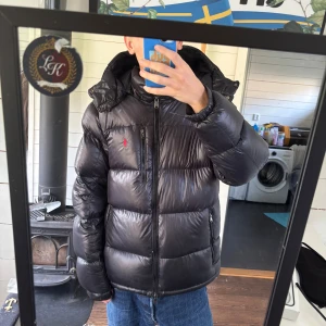 Svart pufferjacka Polo Ralph Lauren - Svart pufferjacka från Polo Ralph Lauren. Tillverkad i polyester och dun och varan har använts flitigt. Jackan görs ren och fixas innan den skickas iväg. Nypris på jackan är runt 5000 kronor.