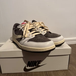 Nike Air Jordan 1 Low OG Olive 43 - Nike Air Jordan 1 Low OG i färgen olive och vitt med svarta detaljer. Snygg retrostil med beige snörning, röd broderad logga på hälen och klassisk swoosh. Ovandel i skinn och mocka, platt sula och rund tå. Perfekt för dig som vill sticka ut med en ikonisk sneaker.