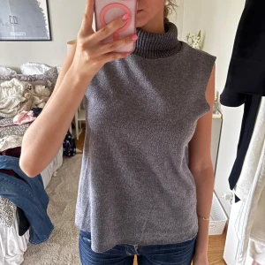 Grå ärmlös polotopp från Zara - Säljer en grå ärmlös polotopp i mjukt stickat material. Toppen har en hög, ribbad polokrage och en rak, loose passform som ger en chill vibe. Perfekt att styla med jeans eller kjol för en enkel men snygg look.