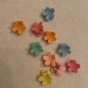 Färgglada blomformade små hårklämmor - Säljer ett gäng söta hårklämmor i form av blommor i olika färger som blå, rosa, gul, orange och grön. Perfekta för att ge din look en lekfull och färgstark touch. Blommorna har en matt finish och är små och lätta att bära.