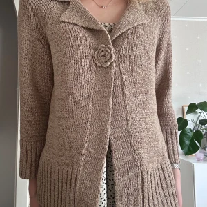 Trekvartsärmad kofta med blomknapp - Stickad kofta med krage och en unik virkad blomknapp framtill. Storlek 42 men passar mig som normalt har S.