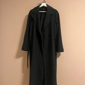 Svart/grå ullkappa från BikBok, stl S - Stilren svart/grå kappa från BikBok i ullblandning. Lång modell med klassisk krage, knäppning framtill och bälte i midjan. Perfekt för dig som vill ha en tidlös och snygg look under höst och vinter. Köpt för 1499 kr, säljer för 650 kr. 