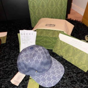 Blå Gucci keps med GG-mönster - Säljer en blå keps från Gucci i storlek S, 56 cm. Kepsen har det klassiska GG-mönstret i ljusblått över hela och justerbar rem i blått skinn baktill. Materialet är bomull och skinn, och kepsen kommer med originalförpackning och kvitto.