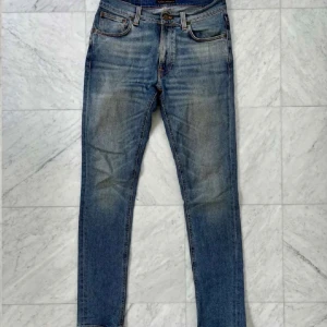 Nudie Jeans lean dean W29 L32 - Säljer ett par klassiska blå slim fit jeans från Nudie Jeans med snygga slitningar och orangea sömmar. Jeansen har fem fickor, normal midja och ikonisk våg på bakfickan. Perfekt passform för dig som gillar en smal siluett.