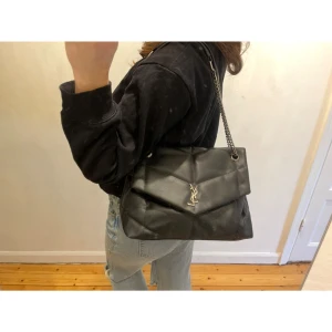 Svart axelväska med kedja - Snygg svart axelväska med quiltad design och kedjedetaljer. Väskan har en elegant logotyp framtill och är perfekt för att ge en stilren touch till din outfit. Skriv för fler bilder/frågor 