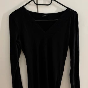 Svart långärmad topp med spets Gina Tricot - Svart långärmad topp från Gina Tricot med v-ringning och bred spetskant runt halsen. Toppens material är mjukt och stretchigt, perfekt för en stilren look. Passformen är normal och toppen är enkel att matcha med olika outfits.