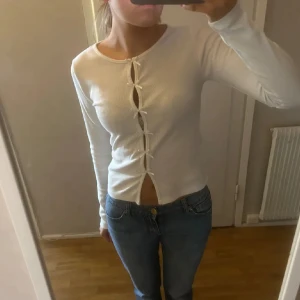 Vit topp  - Supersöt vit långärmad topp från Nelly med ribbad struktur och dekorativa rosetter längs hela framsidan. Slutsåld! Använd fåtal gånger🤗